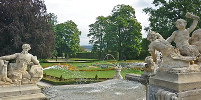 A fountain with statues in front of a manicured green garden - Castle Gardens, Czech Republic