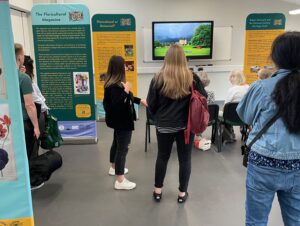 A group of visitors watching a video clip, surrounded by exhibition banners for the Celebrating Marnock Festival at Sheffield Botanical Gardens