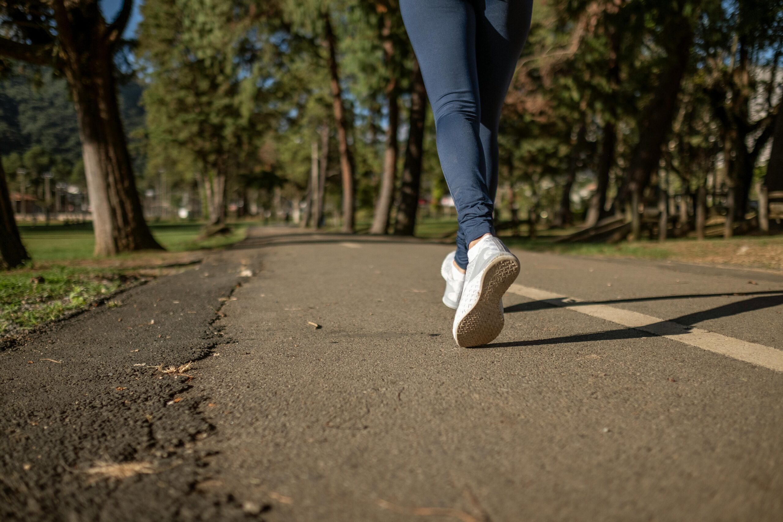 Close up view of someone running along a path in a park, wearing white trainers and blue trousers.